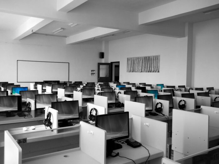 Black and white image of a room with several computers arranged in rows. Some of the computers have lit up blue screens.